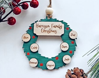 May include: A green and brown wooden Christmas ornament shaped like a wreath with the text "Harrison Family Christmas" on the top. The wreath has red dots and smaller circles with names written on them, including "Mom", "Dad", "Caleb", "Owen", "Jade", "Hannah", and "Jaycee".