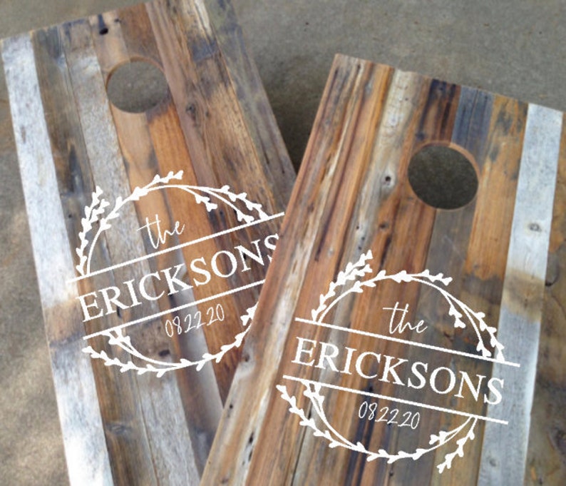 Puede incluir: Dos tableros de juego de lanzamiento de sacos de ma&iacute;z de madera con un aspecto r&uacute;stico y desgastado. Cada tablero presenta un agujero circular y un gr&aacute;fico blanco con el texto "the ERICKSONS" y la fecha "09.22.20" en un dise&ntilde;o de corona decorativa.
