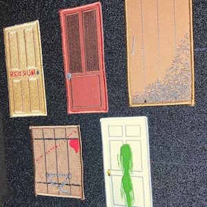 May include: Five embroidered patches depicting different doors. The doors are all different colours and have different designs. One door has the word "REDRUM" written on it in reverse. Another door has a green figure inside.