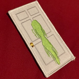 May include: White embroidered patch with a green figure standing in a doorway. The figure is dripping and appears to be a ghost.