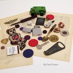 May include: A collection of vintage and modern trinkets, including a green toy van, a matchbook, a lighter, a spoon, a bottle opener, a key, buttons, a small toy airplane, a heart-shaped charm, a small figure of a person, and a variety of other small objects. The objects are arranged on a piece of paper with the words "My Dust Drawer" written at the bottom.