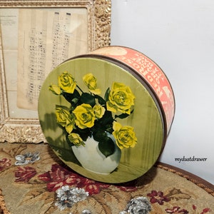 May include: Vintage round tin box with a green background and a floral design of yellow roses in a white vase. The text on the lid reads "The Rose of Sharon".