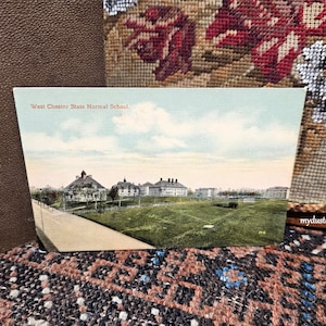 May include: Vintage postcard showing a view of West Chester State Normal School. The postcard is in color and shows a large building with a grassy field in front of it.