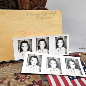 May include: Vintage black and white photo booth strip of a young person in a collared shirt. A tan envelope with handwritten text is behind the photos. A small American flag is in the foreground.