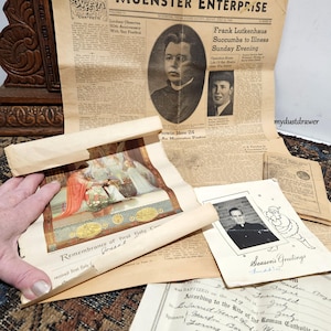 May include: A collection of vintage paper documents, including a newspaper clipping with the headline "Frank Lutkenhaus Succumbs to Illness Sunday Evening", a religious certificate with the text "Remembrance of first holy Communion", a Christmas card with the text "Season's Greetings", and a baptism certificate with the text "According to the Rite of the Roman Catholic Church".