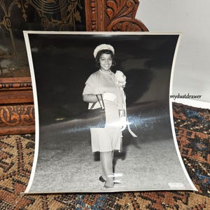 May include: Black and white photograph of a woman in a dress, hat, and gloves, holding a purse and a bouquet. The photograph is slightly curved, with the text "mydustdrawer" in the corner.
