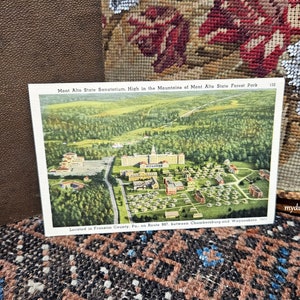 May include: An aerial view postcard of the Mont Alto State Sanatorium, located in the mountains of Pennsylvania. The postcard reads "Mont Alto State Sanatorium. High in the Mountains of Mont Alto State Forest Park. Located in Franklin County, Pa. on Route 957 between Chambersburg and Waynesboro."