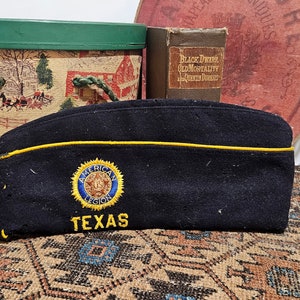 May include: A dark blue military-style hat with a yellow trim and an embroidered American Legion patch that says "Texas".