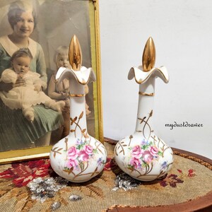 May include: Pair of white porcelain perfume bottles with gold accents and floral designs. The bottles have a gold top with a pointed finial. The bottles are decorated with pink roses, gold vines, and blue flowers.
