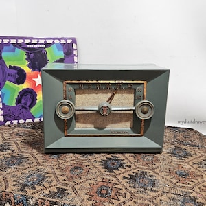 May include: Vintage teal Crosley radio with gold accents and a tan speaker cover. A Steppenwolf album is propped up next to the radio. The radio has a tuning dial and two knobs. The radio is sitting on a patterned rug.