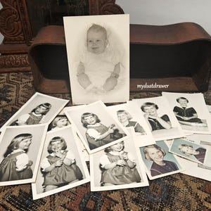 May include: A collection of vintage black and white photographs of children. The photos are arranged in a pile on a patterned surface. The photos feature children in various poses and clothing.