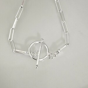 May include: A silver bracelet with a toggle clasp. The bracelet is made of a chain with oval links.