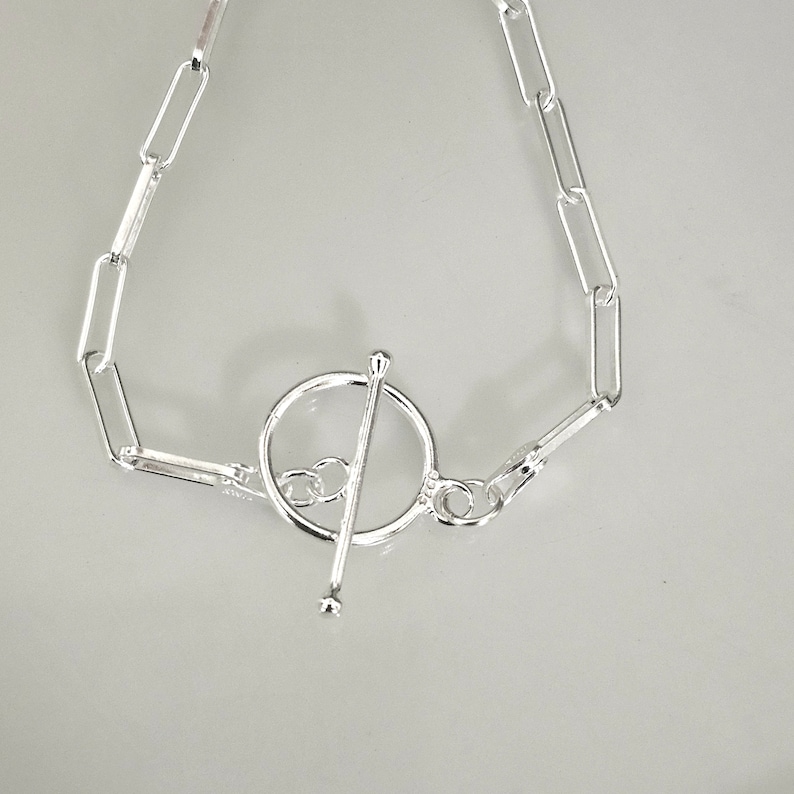 May include: A silver bracelet with a toggle clasp. The bracelet is made of a chain with oval links.