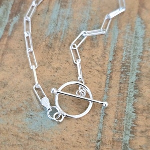 May include: Silver chain necklace with a toggle clasp. The chain is made of linked ovals.
