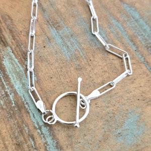May include: A silver chain bracelet with a toggle clasp. The chain is made of small, rectangular links.