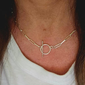 May include: A silver chain necklace with a toggle clasp. The chain is made of small, rectangular links.