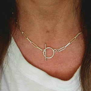 May include: A silver chain necklace with a toggle clasp. The chain is made of small, rectangular links.
