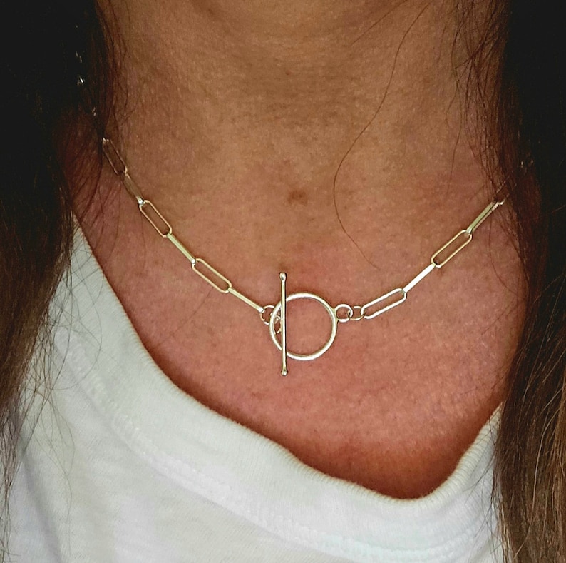 May include: A silver chain necklace with a toggle clasp. The chain is made of small, rectangular links.