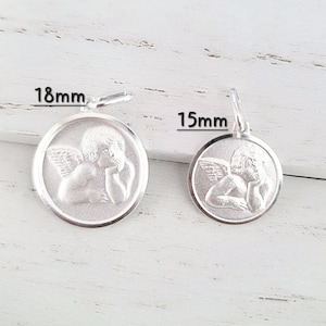 May include: Two silver-colored pendants, one 18mm and the other 15mm in diameter, each featuring a detailed relief of a cherub with wings. The cherubs are in a contemplative pose. The pendants have a loop for hanging.