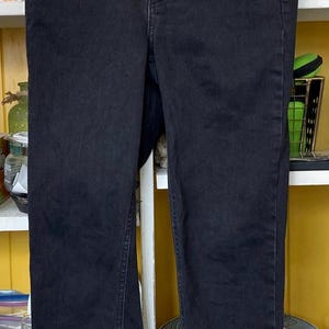 Pu&ograve; includere: Jeans skinny neri a vita alta con zip. I jeans hanno un aspetto leggermente rovinato e sono appesi a un'appendiabiti nero.