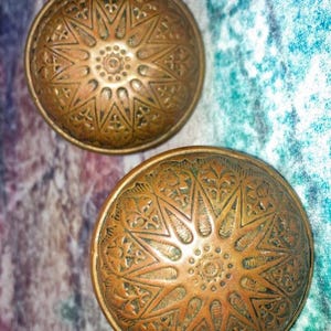 Puede incluir: Dos objetos decorativos abovedados de color bronce antiguo. Cada uno tiene un intrincado patrón de estrella con detalles florales y geométricos. Probablemente vintage o de inspiración vintage.