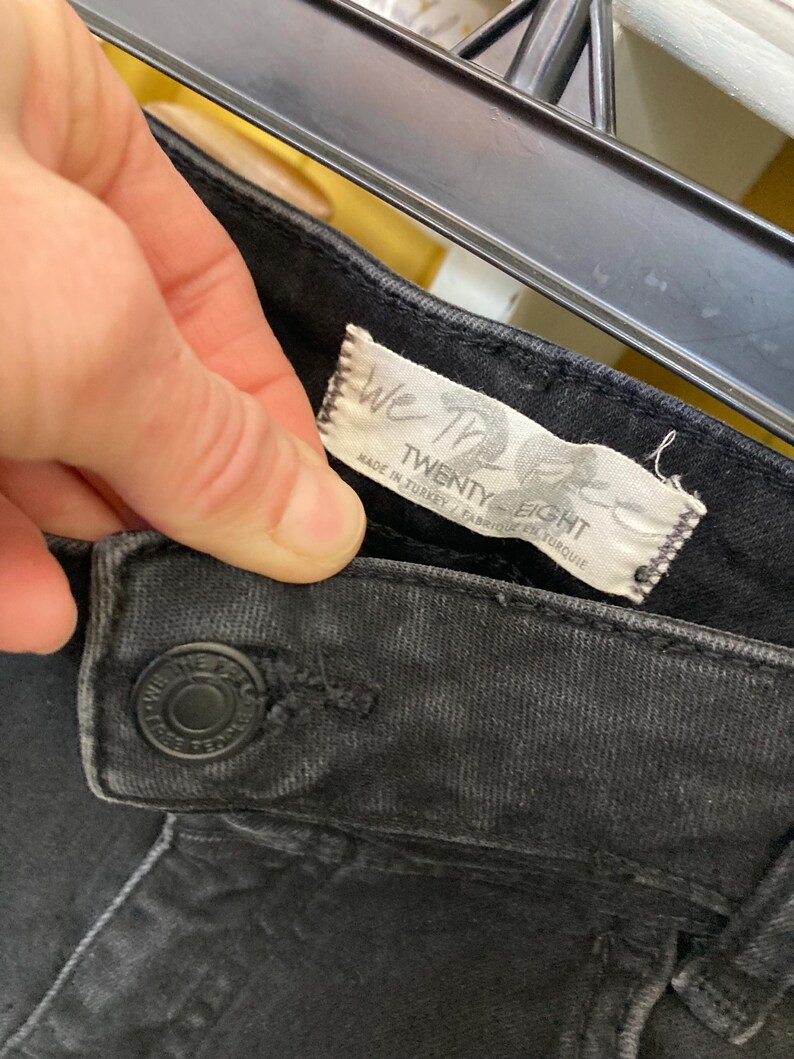 Pu&ograve; includere: Jeans in denim nero con un'etichetta bianca che recita "We The Free Twenty Eight" e "Made in Turkey / Fabrique en Turquie".