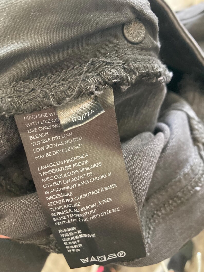Pu&ograve; includere: Un'etichetta di cura nera con testo bianco che dettaglia le istruzioni di lavaggio. Il testo include "Machine Wash with Like Colors", "Use Only No Bleach", "Tumble Dry Low", "Low Iron as Needed", "May Be Dry Cleaned", "Lavage en Machine &agrave; Temp&eacute;rature Froide", "Avec Couleurs Similaires", "Utiliser un Agent de Blanchiment Sans Chlore Si N&eacute;cessaire", "S&eacute;cher par Culbutage &agrave; Basse Temp&eacute;rature", "Repasser, au Besoin, &agrave; Tr&egrave;s Basse Temp&eacute;rature", "Peut-&ecirc;tre &ecirc;tre Nettoy&eacute;e Sec", "冷水机洗", "与同色一起", "仅使用无需漂白剂", "低温烘干", "低温熨烫", "可干洗".