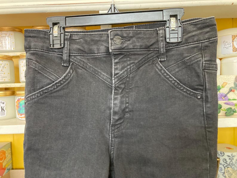 Pu&ograve; includere: Jeans in denim nero a vita alta e gamba dritta. I jeans hanno una chiusura con bottoni e passanti per la cintura.