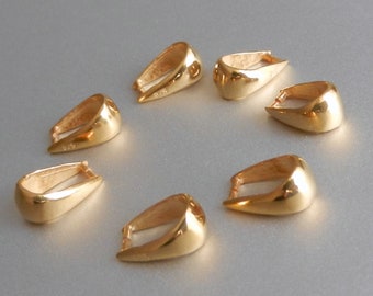 Pode incluir: Sete argolas de pendente de metal dourado, cada uma com uma forma e tamanho ligeiramente diferentes. As argolas estão dispostas em círculo sobre uma superfície cinza claro.