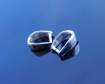 Puede incluir: Dos cierres de joyería de metal plateado, cada uno con una forma redondeada ligeramente curvada. Los cierres están sobre una superficie azul.