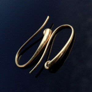 May include: A pair of gold-toned earring hooks. The hooks are made of a smooth, rounded metal and have a simple, elegant design.