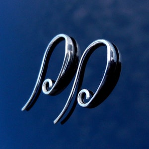 May include: A pair of silver hoop earrings with a unique, curved design. The earrings are made of a smooth, shiny metal and have a simple, elegant look.