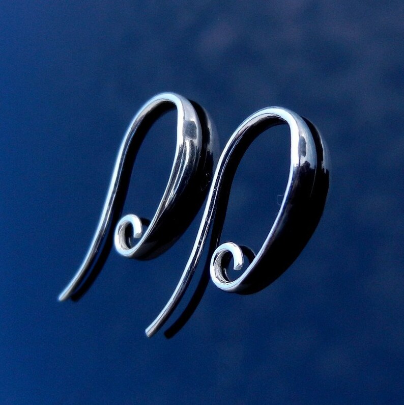 May include: A pair of silver hoop earrings with a unique, curved design. The earrings are made of a smooth, shiny metal and have a simple, elegant look.