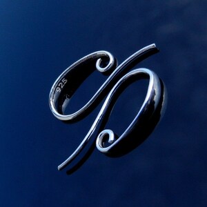 May include: A silver sterling silver 925 charm in the shape of a stylized percent sign. The charm is on a dark blue background.