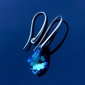 May include: A pair of silver dangle earrings with a blue crystal teardrop pendant.