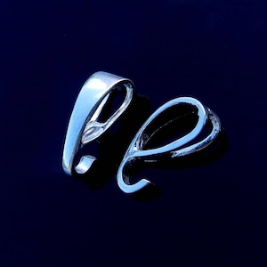 Puede incluir: Dos baúles de colgante plateados, uno con un diseño de bucle simple y el otro con un diseño de doble bucle más intrincado.