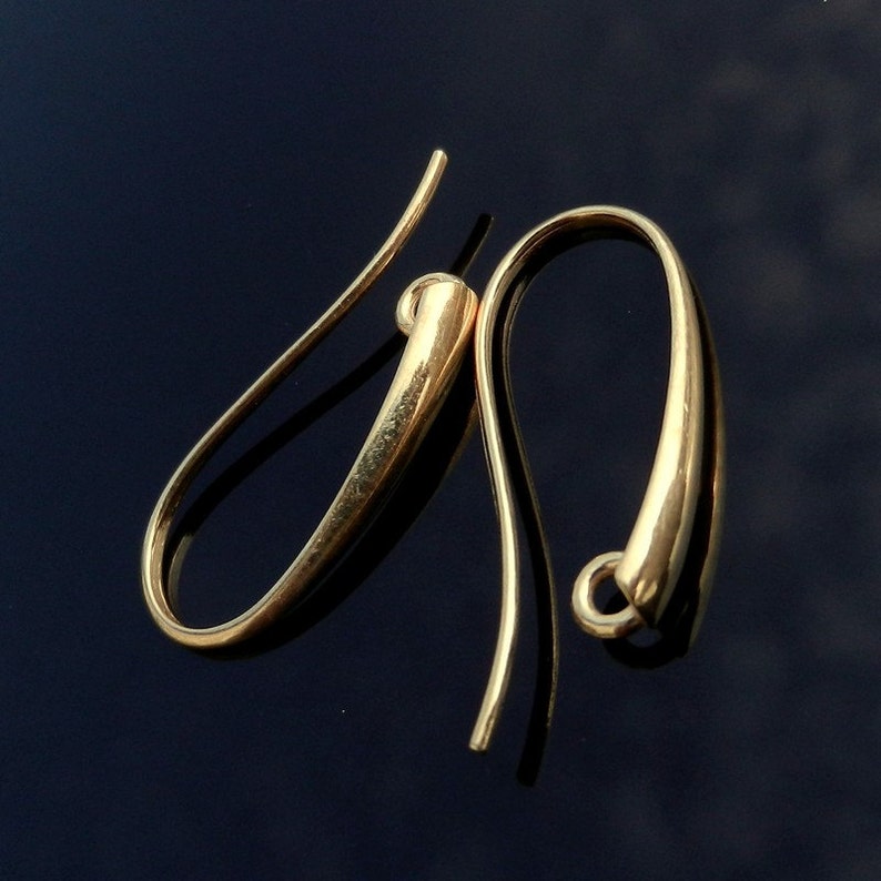 May include: A pair of gold-toned earring hooks. The hooks are made of a smooth, rounded metal and have a simple, elegant design.