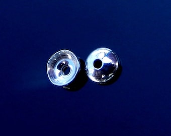 May include: Two shiny, silver-colored metal beads with a reflective surface. One bead is a cup shape, and the other is a sphere with a hole. The beads are set against a dark blue background.