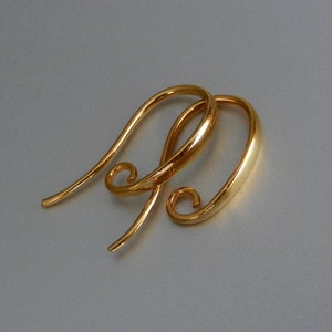 May include: A pair of gold-toned earring hooks with a curved design. The hooks have a small loop at the end.