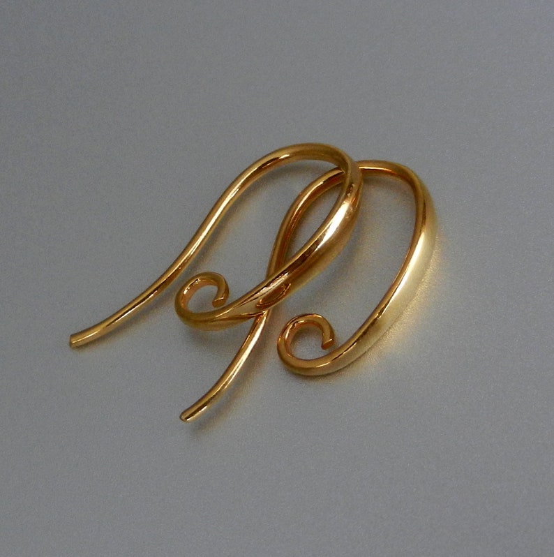 May include: A pair of gold-toned earring hooks with a curved design. The hooks have a small loop at the end.