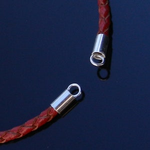Op de afbeelding: Een rood leren koord met zilveren metalen eindkappen. De eindkappen hebben een lus om een ​​hanger of bedel aan te bevestigen.