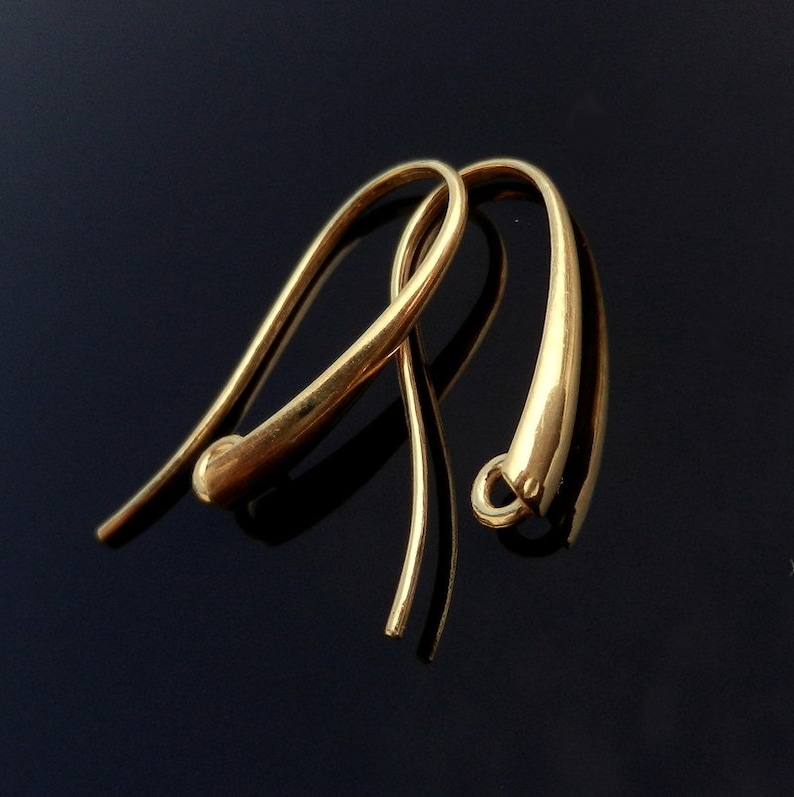 May include: A pair of gold-toned earring hooks. The hooks are made of a smooth, rounded metal and have a simple, elegant design.