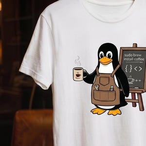 May include: A white t-shirt featuring a graphic of a penguin wearing a brown apron and holding a coffee mug. Next to the penguin is a chalkboard with the text "sudo apt-get install coffee" and code symbols. The shirt has short sleeves and a crew neck.
