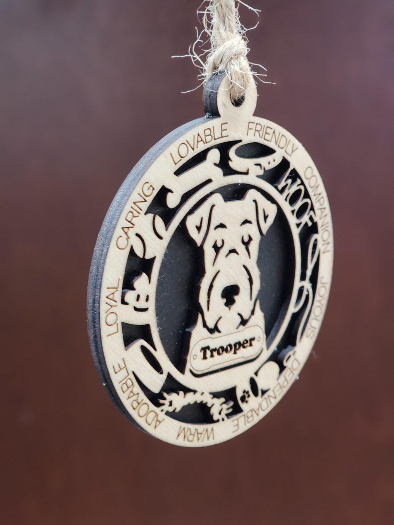 May include: A wooden ornament with a silhouette of a dog's head and the words "Loyal, Caring, Lovable, Friendly, Warm, Adorable, Dependable, Joyous, Companion, Woof" around the edge. The dog's name "Trooper" is written on a tag.