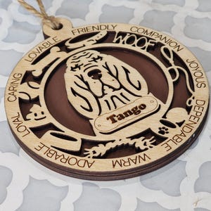 May include: A wooden ornament shaped like a dog with the words "Woof" and "Tango" on it. The ornament is decorated with the words "caring, loyal, lovable, friendly, companion, joyous, dependable, warm, adorable".