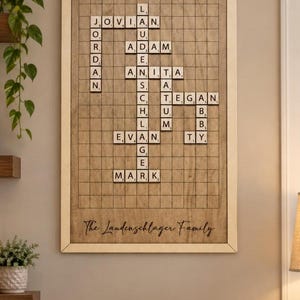 May include: A rectangular wooden wall art piece featuring a grid resembling a crossword puzzle with letter tiles spelling out names including Jordan, Jovian, Adam, Anita, Tegan, Evan, and Mark. The text The Laudenschlager Family is printed at the bottom.
