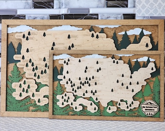 May include: A wooden map of the United States with the National Parks marked with green trees. The map is framed in a light brown wood frame. The text "Our National Park Adventures" is at the bottom of the map.