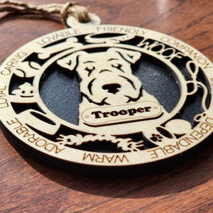 May include: A wooden ornament with a black silhouette of a dog and the words "Loyal, Caring, Lovable, Friendly, Woof, Companion, Joyous, Dependable, Adorable, Warm" around the edge. The dog's name "Trooper" is written on a tag.