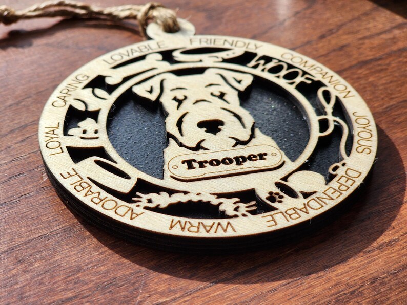 May include: A wooden ornament with a black silhouette of a dog and the words "Loyal, Caring, Lovable, Friendly, Woof, Companion, Joyous, Dependable, Adorable, Warm" around the edge. The dog's name "Trooper" is written on a tag.