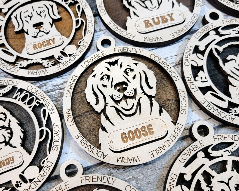 May include: Wooden dog ornaments with personalized names, including Rocky, Ruby, and Goose. Each ornament features a dog breed silhouette with a descriptive word circle around the dog. Words include: "Woof", "Loyal", "Caring", "Friendly", "Companion", "Joyous", "Dependable", "Lovable", "Adorable", and "Warm".